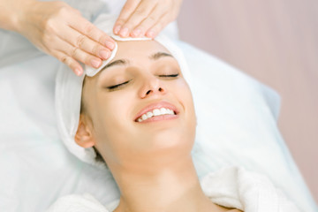 Cosmetologist hands cleanse the skin. Facial skin care. Smiling girl on a relaxing cosmetology...