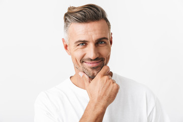 Image of optimistic man 30s with bristle wearing casual t-shirt smiling and touching chin