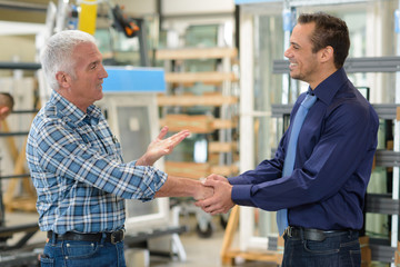 salesman and worker shaking hands in factory