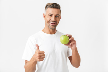Portrait of healthy man 30s having bristle in casual t-shirt posing on camera and holding green apple in hand