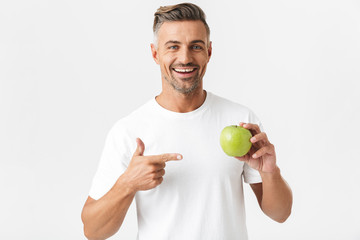 Portrait of attractive man 30s having bristle in casual t-shirt posing on camera and holding green apple in hand