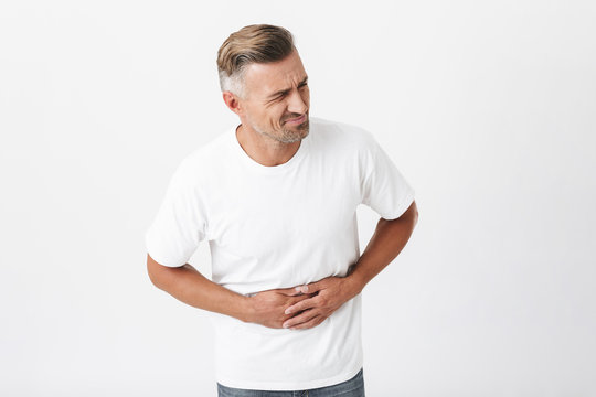 Image of adult man 30s with bristle wearing casual t-shirt touching his belly because of pain