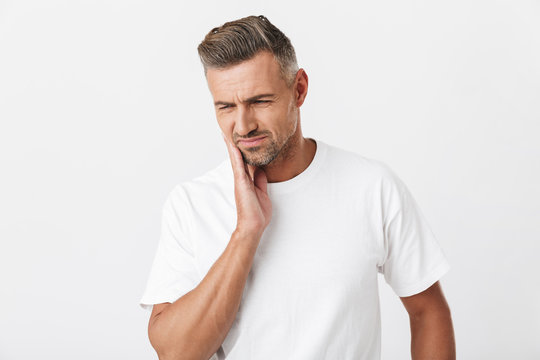 Image of muscular man 30s with bristle wearing casual t-shirt touching his cheek and suffering from toothache