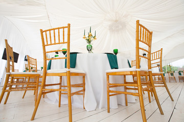 Interior of tent for wedding dinner, ready for guests. Served round banquet table. Golden dishes, green wine glasses and napkins. Catering concept.