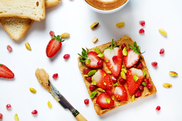 Healthy vegan breakfast concept. Cappuccino, soy milk foam, peanut butter sandwich, toasted bread, pomegranate seeds, pistachio nut. White table background. Top view, close up, copy space, flat lay.