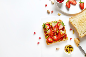 Healthy vegan breakfast concept. Peanut butter sandwich with strawberry, few pieces of toasted bread, pomegranate seeds, pistachio nut. White table background. Top view, close up, copy space, flat lay