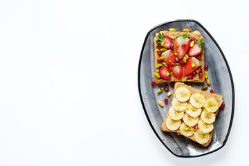 Healthy vegan breakfast concept. Peanut butter sandwiches with strawberry & banana, toasted bread, pomegranate seeds, pistachio nut. White table background. Top view, close up, copy space, flat lay