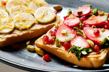 Healthy vegan breakfast concept. Peanut butter sandwiches with strawberry & banana, toasted bread, pomegranate seeds, pistachio nut. White table background. Top view, close up, copy space, flat lay