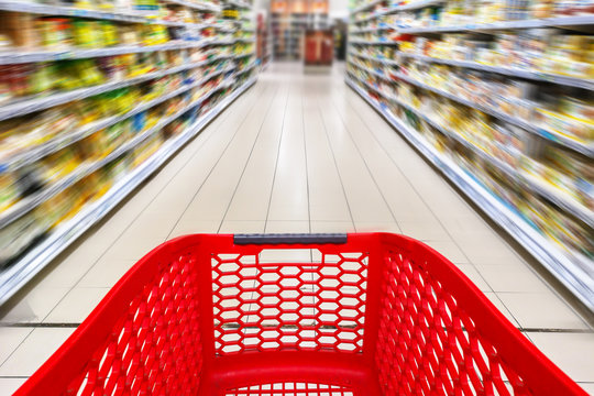 Red empty shopping cart in a supermarket aisle with nobody, motion blur
