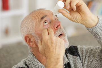 senior man dripping a red eye with eye drops