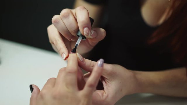 Professional nail artist applies finish layer of clear nail polish on woman's nails with manicure in salon. Master does manicure procedure to a female in the beauty center. Close-up