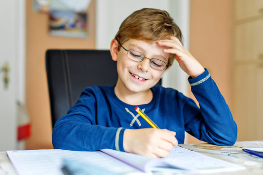 Portrait Of Cute School Kid Boy Wearing Glasses At Home Making Homework. Little Concentrated Child Writing With Colorful Pencils, Indoors. Elementary School And Education