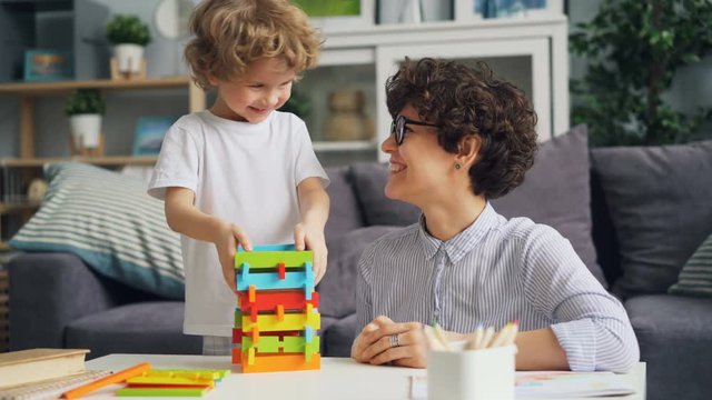 Cheerful girl mom is playing with her little son with wooden blocks and laughing enjoying educational activity. Happy family and interesting toys concept.