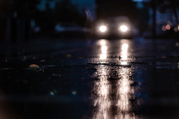 Night road blurred. Headlight of car in the dark while heavy raining. Rain in the city. Road, pavement, close up. Water splashes, spills on roadway