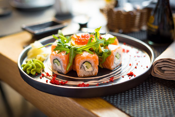 A plate of sushi with salmon, caviar, arugula/rucola/ruccola/rocca salad and wasabi, close up, back view, horisontally.