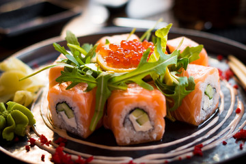 A plate of sushi with salmon, caviar, arugula/rucola/ruccola/rocca salad and wasabi, close up, back view, horisontally.