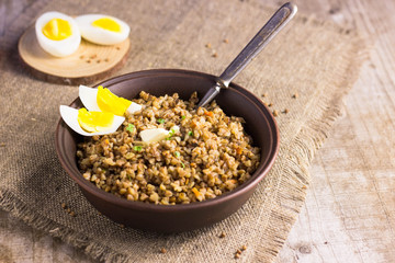 Buckwheat porridge with mushrooms on a plate. Buckwheat porridge in black casserole on wooden background closeup
