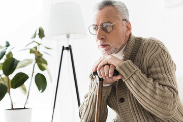 Fototapeta premium thoughtful retired man in glasses holding walking stick