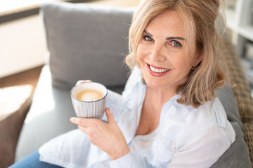 Sympathische ältere Frau genießt zuhause auf der Couch einen Kaffee 