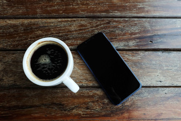 Flat lay photo of smartphone and black coffee on wood table with space for write wording, innovation that change the world such as communication way, business strategies, marketing strategies