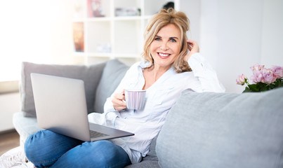 Frau in mittlerem Alter genießt eine Tasse Kaffe zuhause auf der Couch 