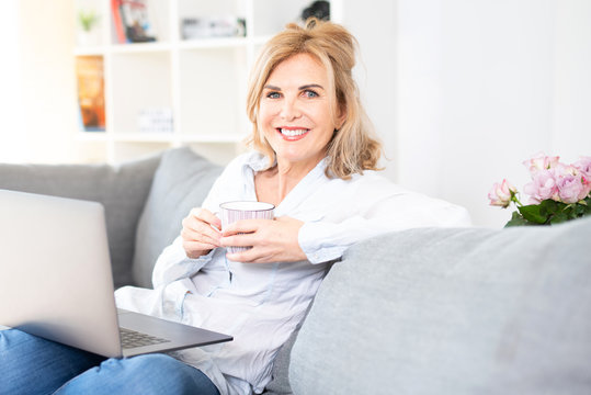 Frau in mittlerem Alter genie&szlig;t eine Tasse Kaffe zuhause auf der Couch 