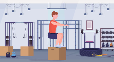 sports man doing box squat exercises guy jumping working out in gym crossfit healthy lifestyle concept modern health club studio interior horizontal