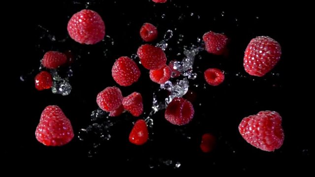 Ripe raspberry with water fly and rotates in the air on a black background