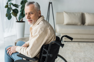 disabled retired man sitting in wheelchair at home and looking at camera