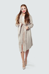 Fototapeta premium Beautiful model woman wearing beige coat and high heels standing against white wall background