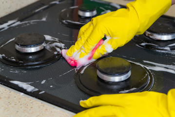 Housewife in colored rubber gloves washes a gas stove with detergent in the kitchen