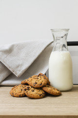 Cookies con pepitas de chocolate y una botella de leche sobre una mesa de madera. Vista de frente. Copy space