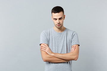 Portrait of angry strict young man in casual clothes looking camera, holding hands crossed isolated on grey wall background in studio. People sincere emotions, lifestyle concept. Mock up copy space.