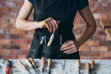 Craftsmanship set arranged on table. Carving and modeling tools. Craft woman in apron choosing chisel. Midsection.
