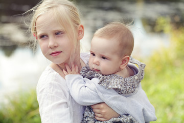 Fototapeta premium Cute little girls sisters outdoor (1 and 8 eyears old)