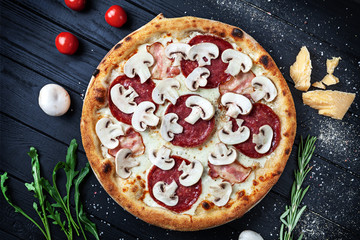 Top view on fresh homemade italian pizza with salami and mushrooms. Pizza, cheese, cherry tomato and parsley on dark wooden background with copy space for design. Top view food menu, recipe