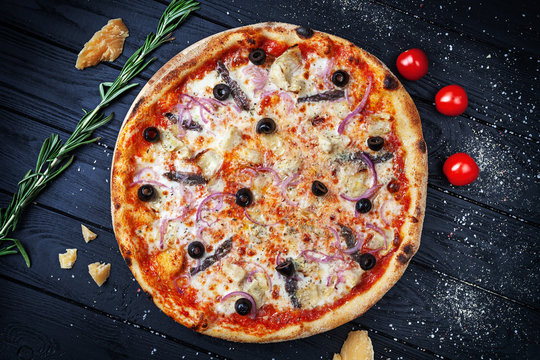 Top view on fresh homemade italian pizza with anchovies. Pizza, cheese, cherry tomato and parsley on dark wooden background with copy space for design. Top view food menu, recipe