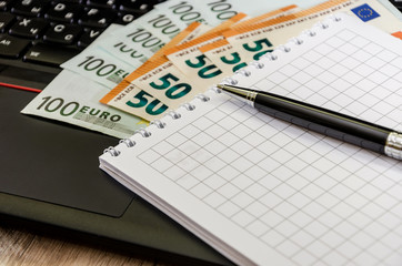 Euro, notebook and pen on the laptop keyboard close up