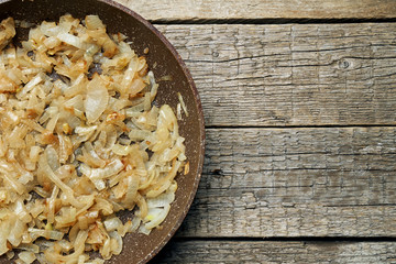 Freshly fried slices of an onion in a stone coated frying pan standing on the wooden boards