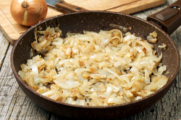 Stone coated frying pan with freshly fried onion on the wooden table