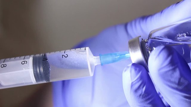 Doctor's hands fill the syringe with vaccine, preparing for the injection of the injection to the patient. Hands close up.