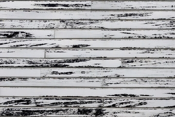 Wooden wall with white paint is severely weathered and peeling