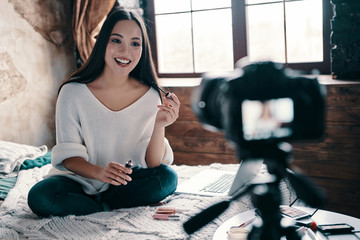 Another video in her vlog. Beautiful young woman holding mascara and smiling while making social...