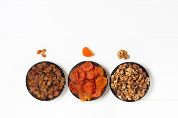 Dried apricot, raisins, walnut in saucers,standing in a row on a white background.