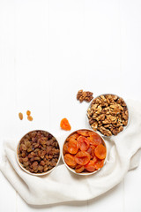 Dried apricots, raisins, walnut in cups standing on a napkin on a white background.