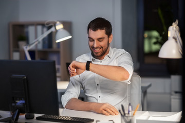 business, technology and time management concept - happy businessman using voice command recorder on smart watch at nigh office
