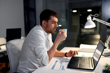 business, deadline and people concept - businessman with laptop computer working and drinking coffee at night office