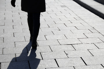 Silhouette of lonely woman walking down the street, black shadow on pavement. Female legs outdoor,...