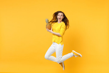 Fototapeta na wymiar Cheerful young woman in casual clothes jumping, hold fresh ripe pineapple fruit isolated on yellow orange wall background in studio. People vivid lifestyle, relax vacation concept. Mock up copy space.