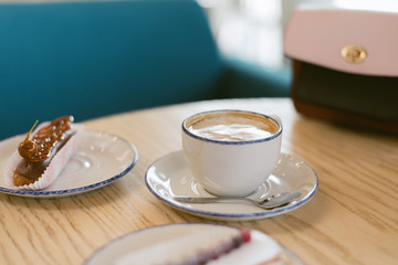 cup of coffee on wooden table. delicious sweet french eclairs and coffee in a coffee shop. Morning breakfast on a light table of a young girl. Coffee, handbag and two eclairs
